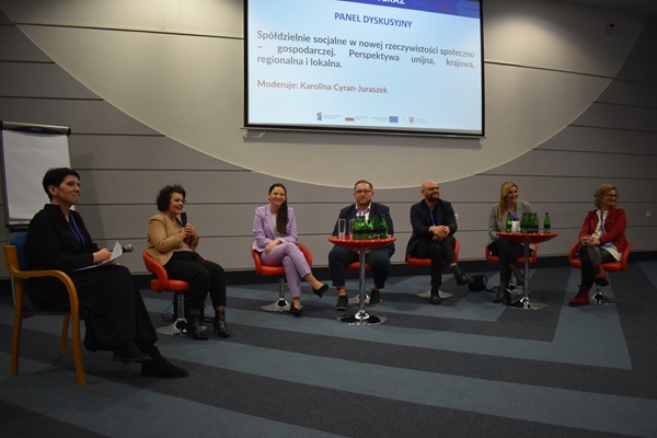 Zdjęcie przedstawiające panelistów - sześć osób + osoba prowadząca panel. W tle prezentacja a w niej slajd z tytułem panelu: "Spółdzielnie socjalne w nowej perspektywie społeczno - gospodarczej. Perspektywa unijna, krajowa, regionalna i lokalna. 